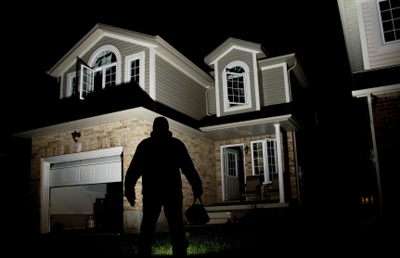 An image of a house at night with a burglar's silhouette used to emphasis the necessity of a home security checklist